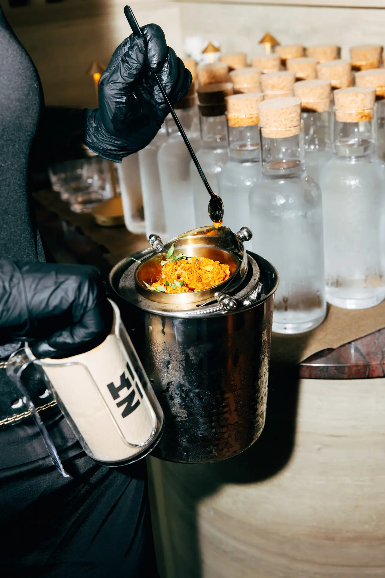 A bartender garnishing a drink beside frosted bottles