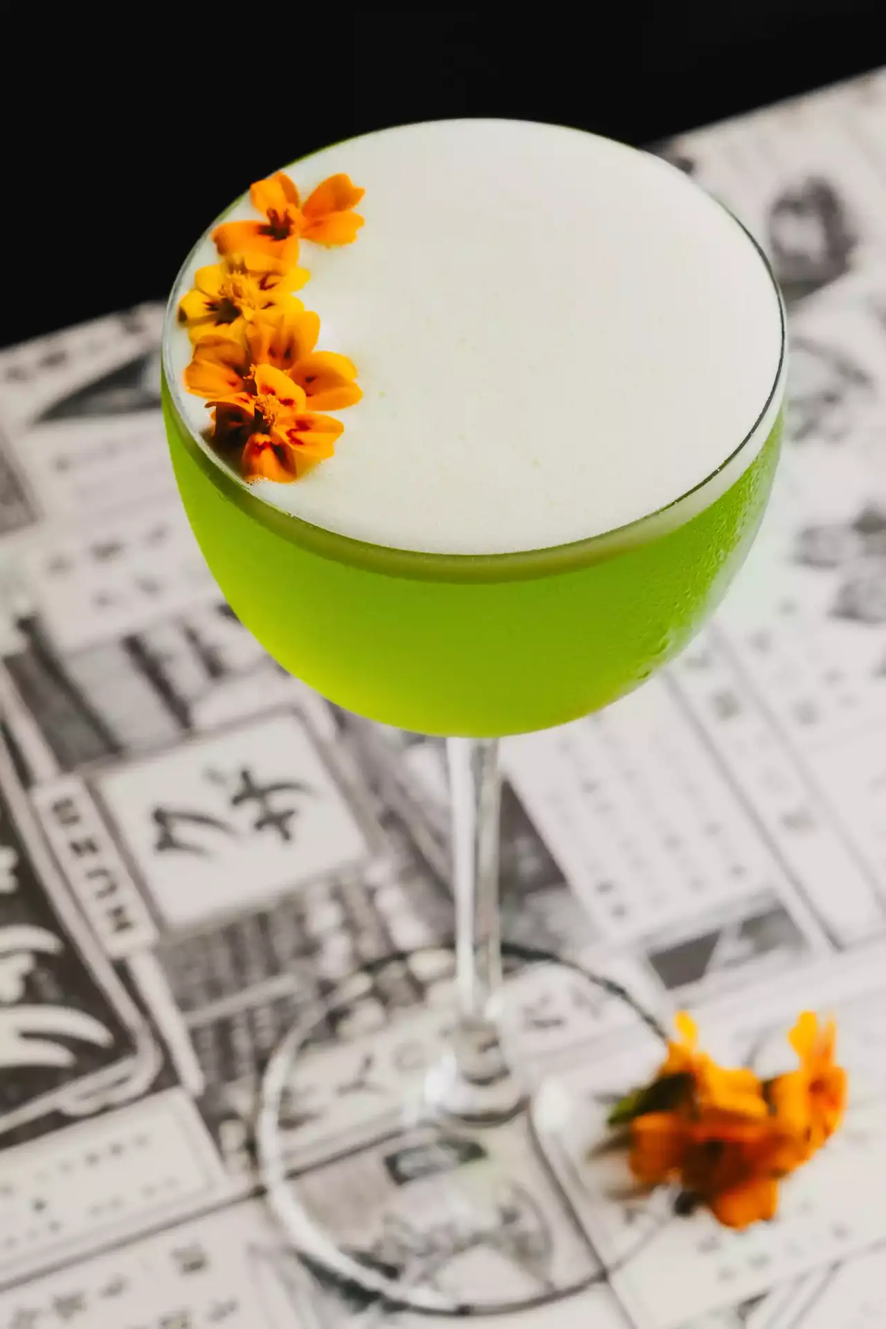A green cocktail with flowers on newsprint at KUZA